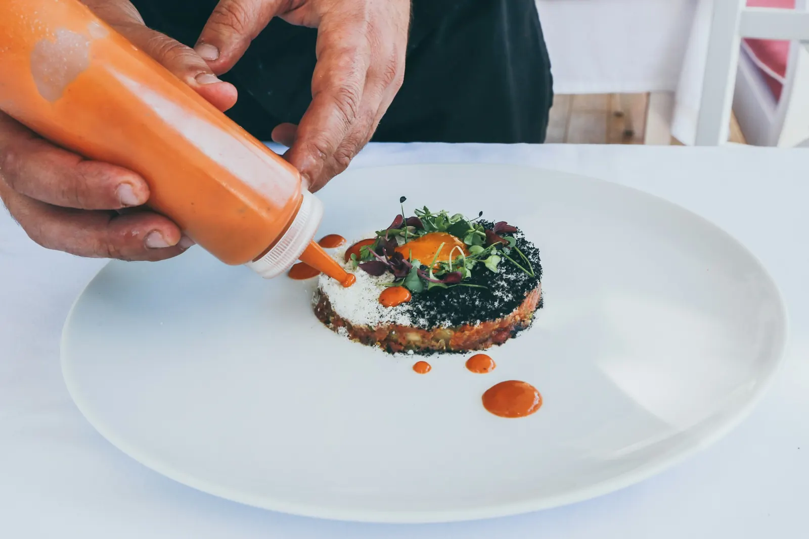 Chef finishing a plated dish with sauce